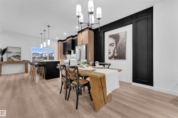 Open-concept dining and kitchen area featuring wood-finish flooring, a modern chandelier, and a black accent wall with decorative paneling - 