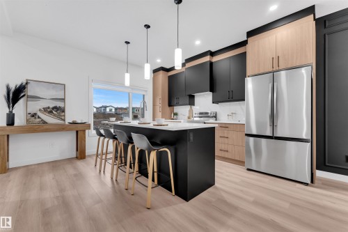 Modern kitchen featuring a large center island with seating, stainless steel appliances, and a mix of black and wood-finish cabinetry - 269 Falcon Crescent, Leduc, AB - Indoor Photo Showing Kitchen With Upgraded Kitchen