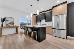 Modern kitchen featuring a large center island with seating, stainless steel appliances, and a mix of black and wood-finish cabinetry - 