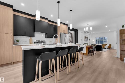 Open-concept kitchen featuring a spacious island with seating, two-tone cabinetry with light wood-finish and matte black panels, stainless steel appliances, and wood-finish flooring - 269 Falcon Crescent, Leduc, AB - Indoor Photo Showing Kitchen With Upgraded Kitchen