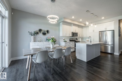 Bright kitchen and dining area featuring white cabinetry, stainless steel appliances, a center island with sink, and wood-finish flooring - 1440 Darby Green, Edmonton, AB - Indoor