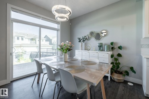Dining area featuring a modern chandelier, dark wood-finish flooring, and a large sliding glass door opening to an outdoor deck - 1440 Darby Green, Edmonton, AB - Indoor Photo Showing Dining Room
