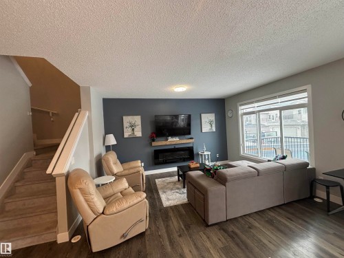 Spacious living area featuring wood-finish flooring, a contemporary electric fireplace with a floating mantel, and a large window with white trim - 1440 Darby Green, Edmonton, AB - Indoor Photo Showing Living Room