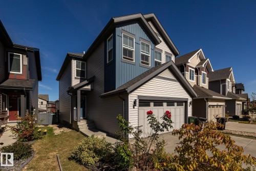 Contemporary two-story exterior featuring a two-tone siding facade, prominent front-facing garage, covered entryway, and asphalt shingle roofing - 1440 Darby Green, Edmonton, AB - Outdoor With Facade