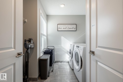 Dedicated laundry room featuring full-size front-loading appliances, a single window, overhead lighting, and tile flooring - 1440 Darby Green, Edmonton, AB - Indoor Photo Showing Laundry Room