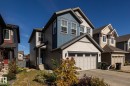 Contemporary residential exterior featuring a multi-tone facade with blue and grey siding, a front-facing attached garage, a covered entryway, and a paved driveway - 1440 Darby Green, Edmonton, AB  - Outdoor With Facade 