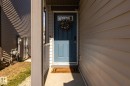 Entryway featuring a blue paneled door with a rectangular window, light beige horizontal siding, a concrete porch, and a dark soffit - 1440 Darby Green, Edmonton, AB  - Outdoor With Exterior 