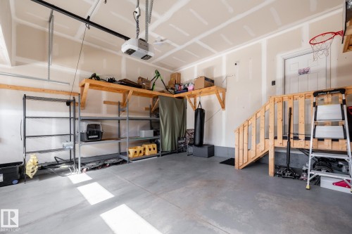 Concrete flooring in a garage space featuring an automatic garage door opener, built-in shelving, a wooden staircase, and overhead storage platforms - 1440 Darby Green, Edmonton, AB - Indoor Photo Showing Garage