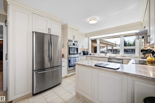 Kitchen featuring white cabinetry, stainless steel appliances, light-toned countertop surfaces, a built-in cooktop, and a large window - 227 Westridge Road, Edmonton, AB - Indoor Photo Showing Kitchen