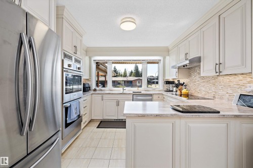 Contemporary kitchen featuring white cabinetry, integrated stainless steel appliances, a tiled backsplash, light-toned countertops, and a window above the sink - 227 Westridge Road, Edmonton, AB - Indoor Photo Showing Kitchen With Double Sink With Upgraded Kitchen
