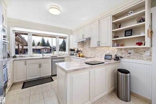 Kitchen featuring white cabinetry, light-toned stone countertops, a tiled backsplash, stainless steel appliances, and a large window overlooking exterior scenery - 227 Westridge Road, Edmonton, AB - Indoor Photo Showing Kitchen