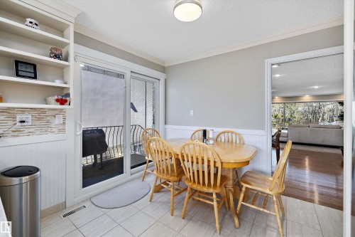 Dining area featuring tile flooring, built-in shelving, a natural stone-look tile backsplash, and a sliding glass door providing access to an outdoor balcony - 227 Westridge Road, Edmonton, AB - Indoor Photo Showing Dining Room