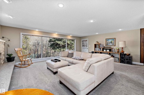 Expansive living area featuring a full wall of windows overlooking a wooded landscape, recessed ceiling lighting, a stone fireplace hearth, and neutral-toned wall paint - 227 Westridge Road, Edmonton, AB - Indoor Photo Showing Living Room