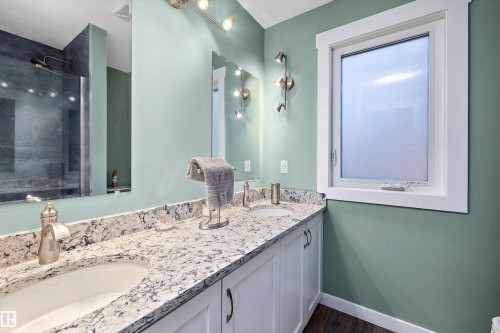 Bathroom vanity featuring dual under-mount sinks with brushed nickel faucets, a speckled stone countertop, and white cabinetry with dark hardware - 227 Westridge Road, Edmonton, AB - Indoor Photo Showing Bathroom
