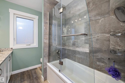 Bathroom featuring a tiled tub-shower combination with a clear glass enclosure, gray stone-look wall tiling, and a built-in shelf - 227 Westridge Road, Edmonton, AB - Indoor Photo Showing Bathroom