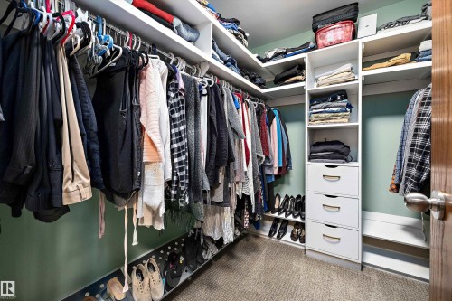 Walk-in closet featuring built-in white shelving, multiple hanging rods, integrated drawers with curved pulls, open shoe storage, and carpeting - 227 Westridge Road, Edmonton, AB - Indoor With Storage