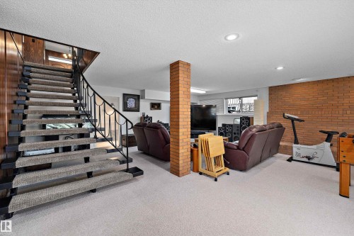 Carpeted staircase with wrought iron railing, leading to a finished lower level featuring brick accent walls, recessed lighting, and soft carpet flooring - 227 Westridge Road, Edmonton, AB - Indoor Photo Showing Other Room