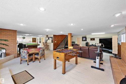 Spacious lower-level entertainment area featuring recessed lighting, a built-in wet bar with seating, exposed brick accents, and a wood-paneled staircase - 227 Westridge Road, Edmonton, AB - Indoor