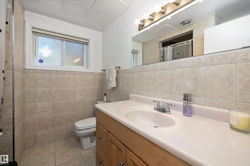 Bathroom featuring a light wood-finish vanity with an integrated sink, a large mirror with vanity lighting, and wall-mounted tile extending to a decorative border - 227 Westridge Road, Edmonton, AB - Indoor Photo Showing Bathroom