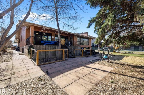 Expansive backyard featuring a large stone patio, a brick exterior, a covered balcony with metal railings, a fenced yard area, and mature trees - 227 Westridge Road, Edmonton, AB - Outdoor With Deck Patio Veranda
