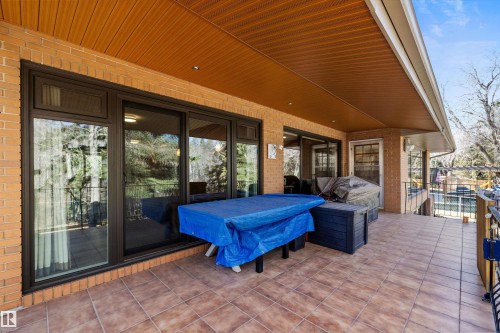 Expansive covered patio featuring brick exterior, tile flooring, a wood-panel ceiling with recessed lighting, and large sliding glass doors - 227 Westridge Road, Edmonton, AB - Outdoor With Deck Patio Veranda With Exterior
