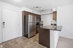 Compact kitchen featuring dark wood cabinetry, stainless steel appliances, a double basin sink, track lighting, and a breakfast bar with a dark countertop - 
