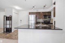 Kitchen featuring dark wood-finish cabinetry, stainless steel appliances, a tile backsplash, and a breakfast bar with a double basin sink and dark countertop - 