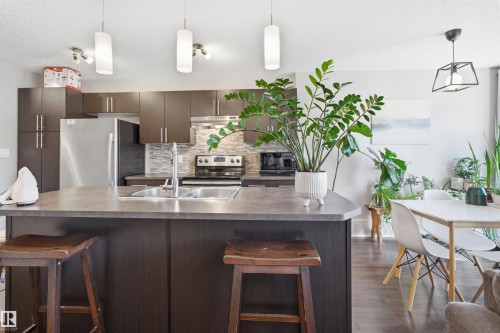 Open-concept living space featuring wood-finish flooring, a kitchen island with pendant lighting, stainless steel kitchen appliances, and recessed ceiling lights - 7323 24 Ave, Edmonton, AB - Indoor Photo Showing Kitchen With Upgraded Kitchen
