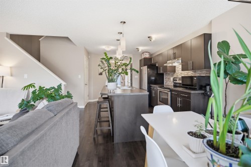Kitchen featuring a large island with an integrated double sink, dark wood-finish cabinetry, stainless steel appliances, and a textured tile backsplash - 7323 24 Ave, Edmonton, AB - Indoor Photo Showing Kitchen With Double Sink With Upgraded Kitchen