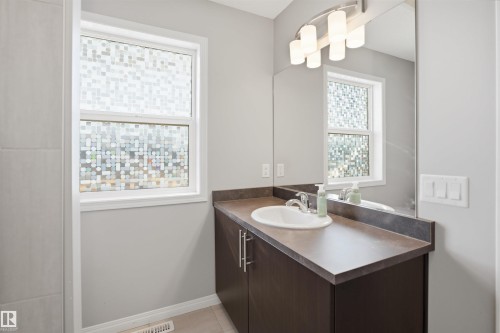 Bathroom featuring a white tub/shower combination with a chrome showerhead, a dark vanity with an integrated sink, a chrome faucet, and a window with frosted glass - 7323 24 Ave, Edmonton, AB - Indoor Photo Showing Bathroom