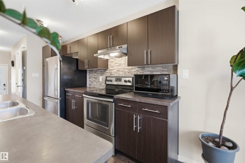 Kitchen featuring dark wood-finish cabinetry, stainless steel appliances, a tiled backsplash, and a double basin sink - 7323 24 Ave, Edmonton, AB - Indoor Photo Showing Kitchen With Double Sink