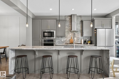 Modern kitchen featuring a waterfall island with a stone-finish countertop, gray cabinetry, stainless steel appliances, and pendant lighting - 1737 Dumont Crescent, Edmonton, AB - Indoor Photo Showing Kitchen With Upgraded Kitchen