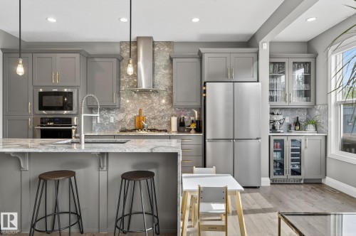 Contemporary kitchen featuring grey cabinetry, stainless steel appliances, a large island with seating, a patterned backsplash, and wood-finish flooring - 1737 Dumont Crescent, Edmonton, AB - Indoor Photo Showing Kitchen With Upgraded Kitchen