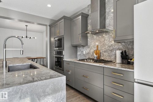 Kitchen featuring grey cabinetry with gold-tone hardware, a stainless steel gas range, built-in microwave and oven, an oversized island with a built-in sink, and a modern industrial-style faucet - 1737 Dumont Crescent, Edmonton, AB - Indoor Photo Showing Kitchen With Upgraded Kitchen
