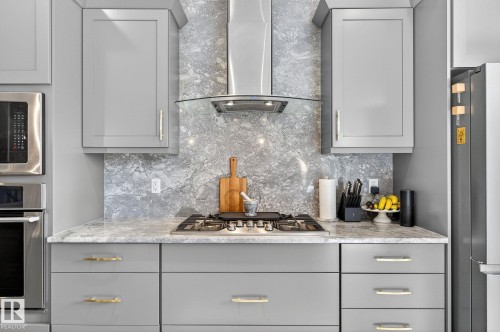 Modern kitchen featuring light gray cabinetry with gold-tone hardware, a stainless steel gas range, and a coordinating range hood - 1737 Dumont Crescent, Edmonton, AB - Indoor Photo Showing Kitchen With Upgraded Kitchen