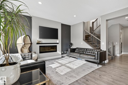 Living area featuring wood-finish flooring, a contemporary built-in fireplace, recessed lighting, and a prominent staircase with dark wood newel posts and railings - 1737 Dumont Crescent, Edmonton, AB - Indoor Photo Showing Living Room With Fireplace