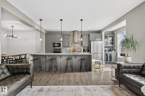 Open-concept kitchen featuring an oversized island with seating, pendant lighting, stainless steel appliances, wood-finish flooring, and gray cabinetry with a complementary tiled backsplash - 1737 Dumont Crescent, Edmonton, AB - Indoor