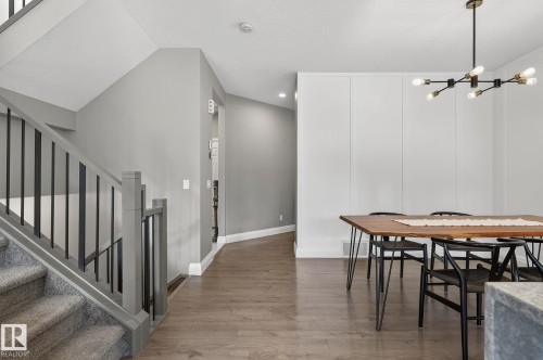 Open-concept area featuring wood-finish flooring, a contemporary chandelier, a white accent wall with vertical paneling, a carpeted staircase with gray newel posts and black balusters, and a recessed lighting fixture - 1737 Dumont Crescent, Edmonton, AB - Indoor