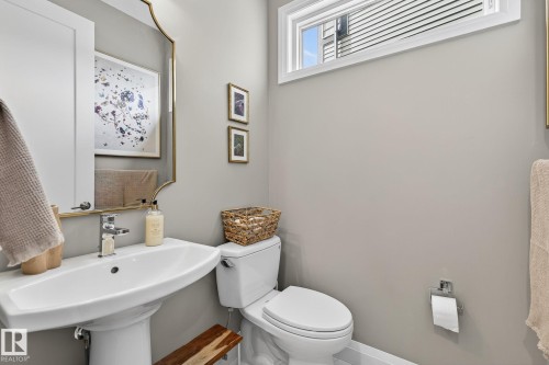 Pedestal sink with polished chrome faucet, rectangular wall mirror with gold-finish frame, and modern white toilet - 1737 Dumont Crescent, Edmonton, AB - Indoor Photo Showing Bathroom