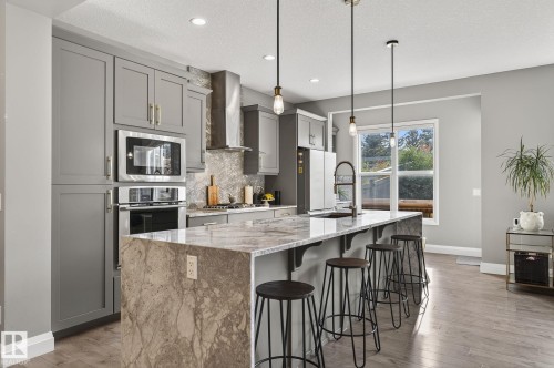 Contemporary kitchen featuring an oversized island with waterfall countertop, pendant lighting, stainless steel appliances, and grey cabinetry - 1737 Dumont Crescent, Edmonton, AB - Indoor Photo Showing Kitchen With Upgraded Kitchen