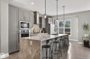 Contemporary kitchen featuring an oversized island with waterfall countertop, pendant lighting, stainless steel appliances, and grey cabinetry - 1737 Dumont Crescent, Edmonton, AB  - Indoor Photo Showing Kitchen With Upgraded Kitchen 