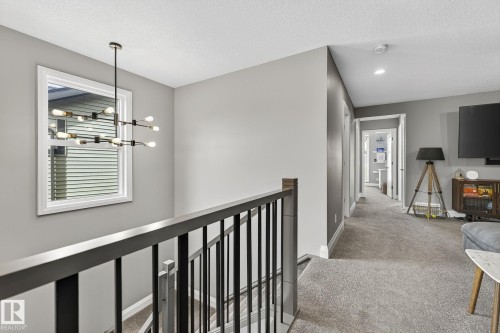 Upper-level landing featuring a contemporary chandelier, a window with white trim, dark wood-finish handrails with black balusters, plush gray carpeting, and recessed lighting - 1737 Dumont Crescent, Edmonton, AB - Indoor Photo Showing Other Room