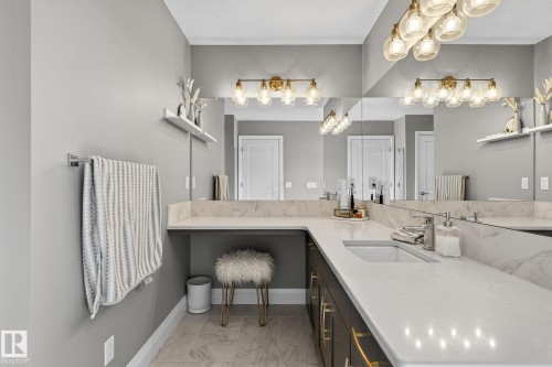 Bathroom vanity featuring an integrated rectangular sink, light-toned countertop, dark wood-finish cabinetry with gold-toned hardware, full-width mirror, and a multi-bulb light fixture - 1737 Dumont Crescent, Edmonton, AB - Indoor Photo Showing Other Room