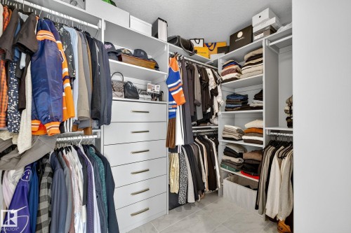 Custom closet system featuring multiple hanging rods, integrated shelving, built-in drawers with gold-tone hardware, and light-toned tile flooring - 1737 Dumont Crescent, Edmonton, AB - Indoor With Storage