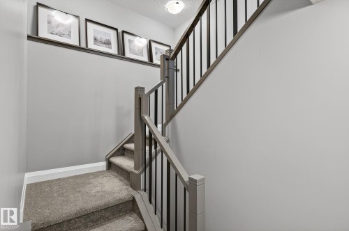 Gray carpeted staircase featuring a gray wood-finish handrail and black metal balusters - 1737 Dumont Crescent, Edmonton, AB - Indoor Photo Showing Other Room
