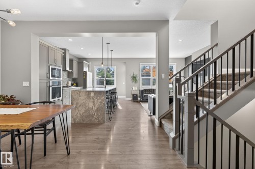 Open-concept living space featuring wood-finish flooring, a modern staircase with dark balusters, a kitchen with grey cabinetry, a waterfall-edge island, and built-in double ovens - 1737 Dumont Crescent, Edmonton, AB - Indoor Photo Showing Dining Room