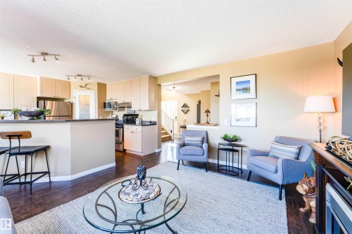 Open-concept living space featuring wood-finish flooring, a kitchen with light cabinetry and stainless steel appliances, and a breakfast bar with a dark countertop - 847 Blacklock Way, Edmonton, AB - Indoor