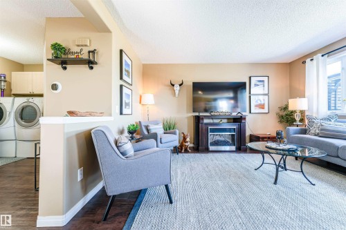 Open-concept living area featuring a built-in electric fireplace with a dark wood mantel, light tan walls, and a window with white curtains - 847 Blacklock Way, Edmonton, AB - Indoor Photo Showing Living Room With Fireplace