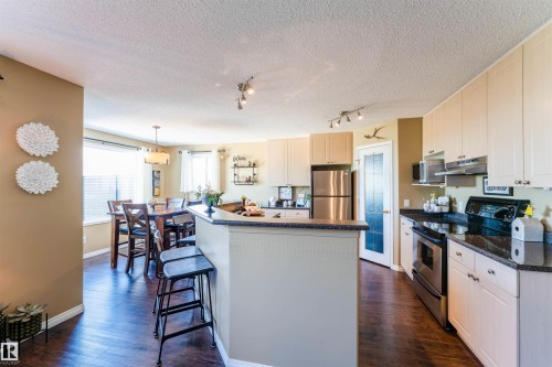 Open-concept kitchen and dining area featuring wood-finish flooring, light-toned cabinetry, stainless steel appliances, dark countertops, and a breakfast bar - 847 Blacklock Way, Edmonton, AB - Indoor Photo Showing Kitchen