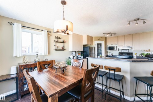 Dining area featuring a wood-finish dining table and coordinated chairs under a contemporary chandelier - 847 Blacklock Way, Edmonton, AB - Indoor Photo Showing Dining Room